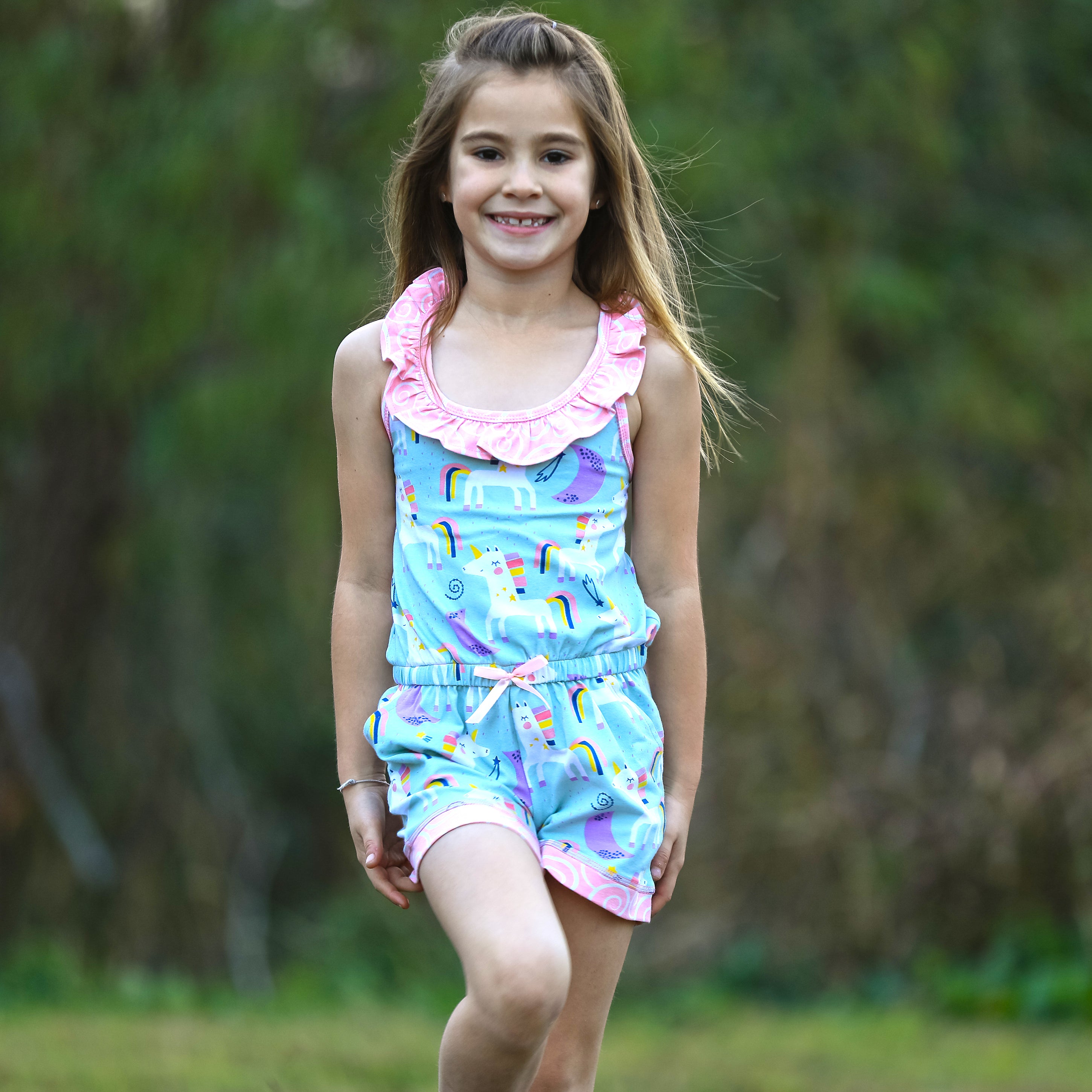 AnnLoren Little & Big Girls Jumpsuit featuring a magical unicorn and rainbow print, with pink swirl ruffle neckline and criss-cross straps.